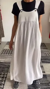 Detailed view of a women's white cotton linen overall dress styled with a black t-shirt