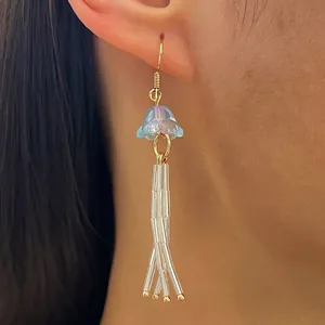 Vue détaillée de boucles d'oreilles à pompons style marin avec fleur et perles.