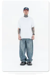 Studiofoto van een man in een oversized wit katoenen t-shirt en een wijde denim spijkerbroek