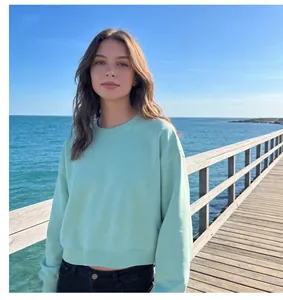 Model wearing a mint green cropped crewneck sweatshirt on a sunny seaside pier.