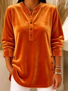 Close-up of orange velvet V-neck top with decorative button details on front and sides.