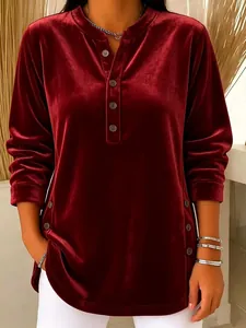 Detail of burgundy velvet long-sleeved top featuring elegant button accents on neckline.
