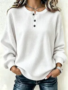 Detailopname van wit sweatshirt met wafelstructuur, zwarte knopen en ronde hals.