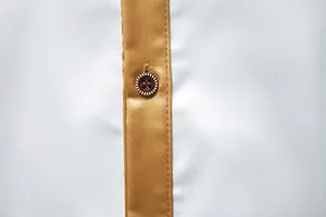 Makroaufnahme des braunen Knopfes und der goldfarbenen Satinleiste an einem weißen Hemd.