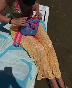 Close-up of shimmering gold sequined straight-leg pants worn in a sunny beach vacation setting