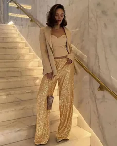 Full-length view of a woman wearing shimmering golden sequin pants on elegant marble stairs.