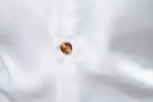 Dettaglio macro di un bottone marmorizzato su camicia di raso bianco dal tessuto setoso