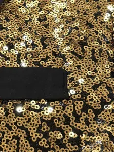 Detailed close-up showing the shiny gold sequins on a black stage performance vest fabric