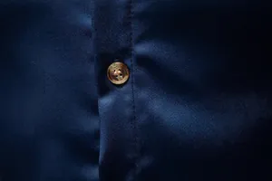 Primo piano della trama del tessuto della camicia in raso blu navy con bottone ambra