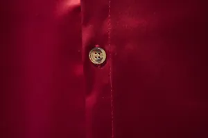 Primo piano del tessuto in raso bordeaux setoso e bottone su una camicia elegante da uomo
