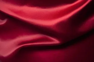 Macro della texture del tessuto di raso rosso con lucentezza setosa ed eleganti drappeggi.