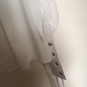 Detailed view of white medieval tunic sleeve featuring metal grommets for lacing