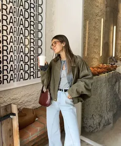 Modern olive green suede bomber jacket with zip-up detail shown in a cafe lifestyle shot.