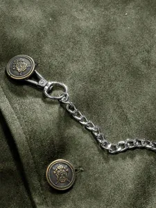 Macro view of olive green suede vest showing vintage crest button and metal chain detail.