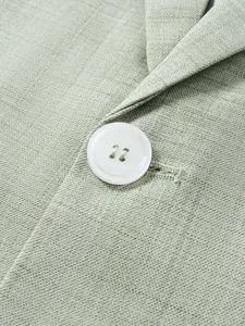 Détail macro d'un bouton blanc et du tissu texturé vert clair d'une veste de costume.