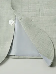 Détail d'un blazer texturé vert clair montrant le bouton blanc et la doublure soyeuse