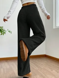 Back view of women's black high-waisted fleece pants in a cozy minimalist room setting.