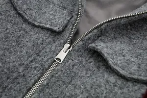 Detailaufnahme einer grauen Tweedjacke mit hochwertigem Metallreißverschluss und Struktur