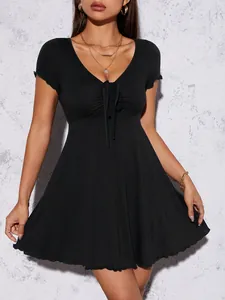 Détail d'une robe courte noire avec col en V, nœud frontal et ourlet à volants.