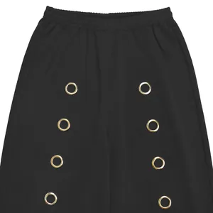 Detail of black wide-leg trousers featuring decorative gold grommets and elastic waist