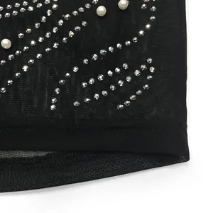 Macro view of rhinestones and pearls on black mesh sheer fabric dress detail