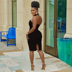 Outdoor street view of a black halter-neck sleeveless bodycon dress with back slit.