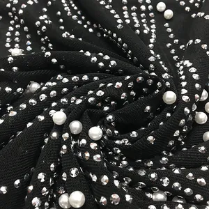 Macro detail of black sheer mesh fabric with sparkling rhinestones and white pearls.