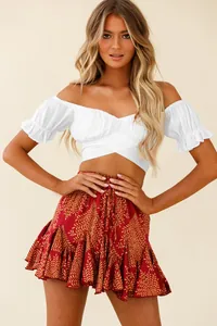 Close-up of white off-shoulder crop top with ruffled sleeves and red printed skirt