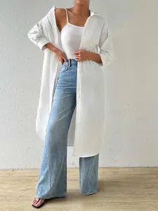 A woman posing in a white longline button-up cardigan shirt with blue wide jeans