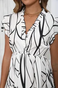 Detail view of a white V-neck dress featuring a black abstract print and elegant ruffle accents