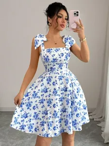 Detailed view of a white summer dress with blue floral print, tie straps, and flared skirt.