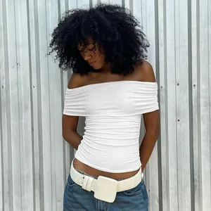 Detail view of a white off-the-shoulder ruched crop top on model against metal wall