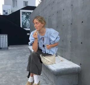 Model wearing a light blue puff sleeve tie front shirt in a stylish urban setting