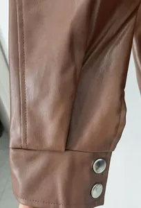 Detailed macro shot of brown faux leather jacket cuff featuring elegant silver metal buttons