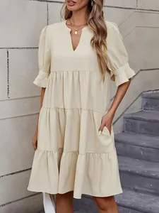 Detalle de vestido corto beige con cuello de pico, mangas abullonadas y bolsillos.