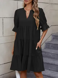 Detalle de vestido negro de capas con cuello en V, volantes y bolsillos