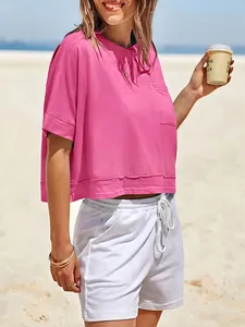 Dettaglio di un crop top rosa oversize con tasca in un ambiente di spiaggia soleggiata.