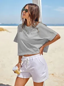 Modella in spiaggia che indossa una maglietta crop grigia oversize e pantaloncini bianchi