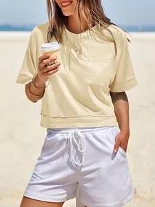 Top corto beige oversize con tasca e pantaloncini bianchi indossato da una donna in spiaggia
