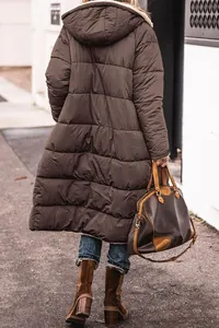 Back view of a stylish long brown hooded puffer coat for women in an urban outdoor setting