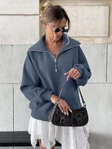Dettaglio styling di una felpa blu da donna con mezza zip e gonna in pizzo bianco.