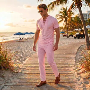 Male model wearing a pink lace-up short-sleeve top and trousers set on a beach at sunset
