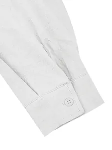Detail view of white cotton linen shirt cuff with button and fine stitching texture.