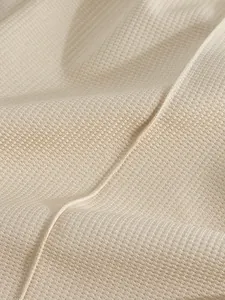 Dettaglio macro del tessuto a nido d'ape traspirante beige per il set sportivo da uomo.