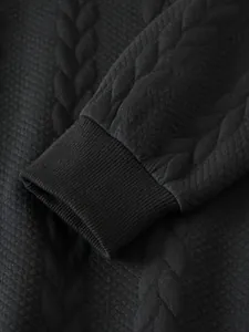 Gros plan du poignet côtelé sur un sweat-shirt noir à maille torsadée texturée.