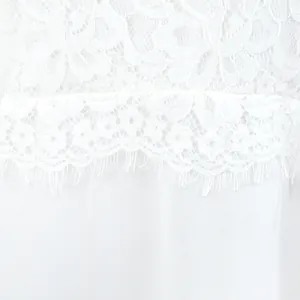 Detailopname van het witte bloemenkant en de verfijnde stoftextuur van de lange jurk.