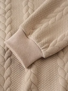 Gros plan d'un sweat-shirt beige montrant le poignet côtelé et la texture matelassée.