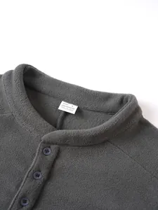Detail van de kraag van een grijs fleece sweatshirt met maatetiket en knopen-detail.