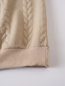 Gros plan du tissu matelassé beige du sweat-shirt montrant la maille torsadée et l'ourlet.