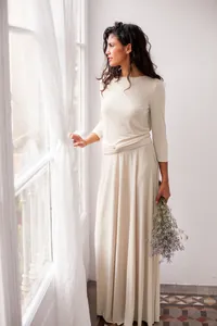 Elegant cream multiway maxi dress with 3/4 sleeves, posing by a window with flowers